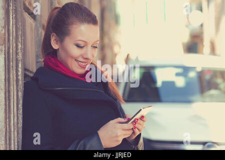 Frau, Lächeln, halten ein Handy steht im Freien neben ihrem neuen Auto-SMS. Stockfoto