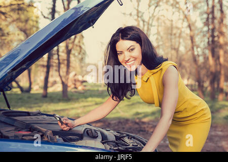 Porträt einer glücklich Frau mit einem Schraubenschlüssel getrost mit ihr Auto auf einem ländlichen Waldpark Hintergrund aufgeschlüsselt Stockfoto