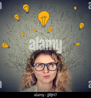 Nachdenkliche Frau in Gläsern mit vielen Ideen, die Glühbirnen über Kopf nach oben isoliert auf graue Wand Hintergrund. Eureka Kreativität Konzept Stockfoto