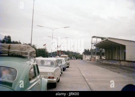 Eine Schlange von Autos wartet einen Checkpoint zwischen Ostberlin und West Berlin während des Kalten Krieges, mit Fahnen von Deutschland, den Vereinigten Staaten und sichtbar an der Vorderseite der Linie, Deutschland, Großbritannien 1970 zu überqueren. Stockfoto