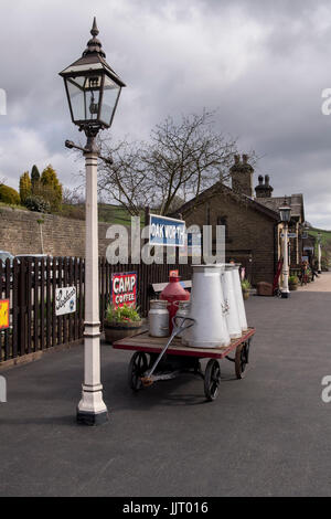 Blick auf die Altstadt Gas Lamp & Milchkannen auf dem Wagen, auf der Plattform am ruhigen, malerischen, historischen Oakworth Station - Keighley und Worth Valley Railway, England, UK. Stockfoto