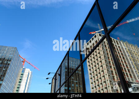 Niedrigen Winkel Ansicht und in der Reflexion von zwei Betonbauten im Bau mit Turmdrehkranen an ihrer Spitze neben einem Glasbau gegen blau sk Stockfoto