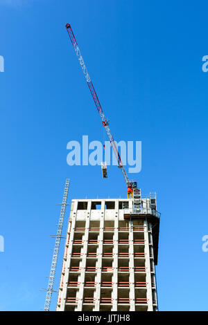 Niedrigen Winkel Blick auf ein konkretes Gebäude im Bau mit einem roten und weißen Turmdrehkran an der Spitze gegen blauen Himmel. Stockfoto