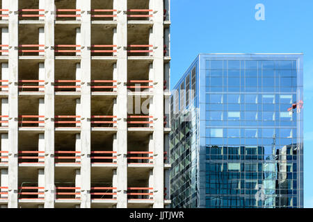 Vorderansicht eines konkreten Gebäude im Bau neben einem Glasbau gegen blauen Himmel. Stockfoto