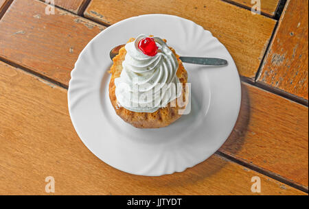 Savarin Kuchen mit Sahne und Sirup, Silberlöffel, weiße Platte auf Holz Hintergrund. Stockfoto