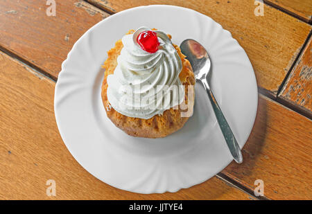 Savarin Kuchen mit Sahne und Sirup, Silberlöffel, weiße Platte auf Holz Hintergrund. Stockfoto