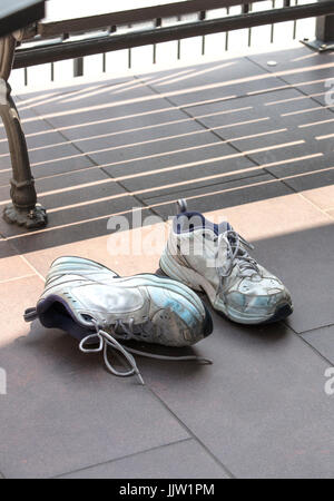 Ein paar alte und gebrauchte Laufschuhe Verlegung auf einem gekachelten Betonboden Straße neben einer Bank Stockfoto