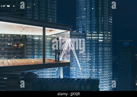 Geschäftsmann in einem modernen Himmel Büro bei Nacht mit Blick auf die schöne Stadt Skyline. Stockfoto