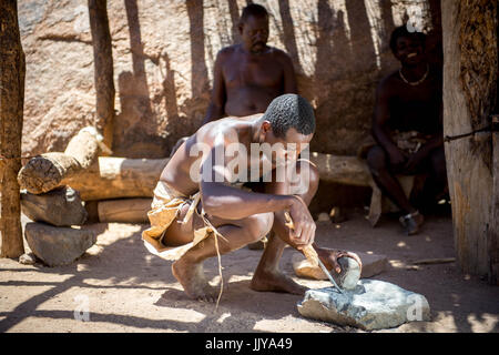 Ein Damara Mann nutzt Werkzeuge und Felsen zum Schärfen eines Messers im Damara Living Museum in Twyfelfontein, gelegen in der südlichen Region von Namibia, Afri Stockfoto