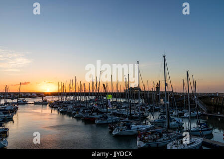 Sonnenaufgang über der Wand von Ramsgate Royal Harbour, mit Silhouette von Yachten im Vordergrund. Himmel mit orange Band entlang der Hafenmauer dann blau. Stockfoto