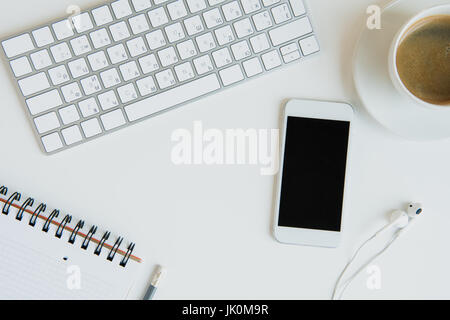 Draufsicht der Tastatur mit Büromaterial und Smartphone auf Tischplatte. Laptop-Schreibtisch-Kaffee Stockfoto