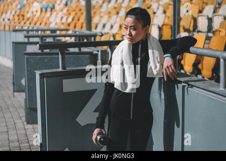 müde asiatischen Sportlerin ruht mit Sport-Flasche und Handtuch auf Stadion Stockfoto