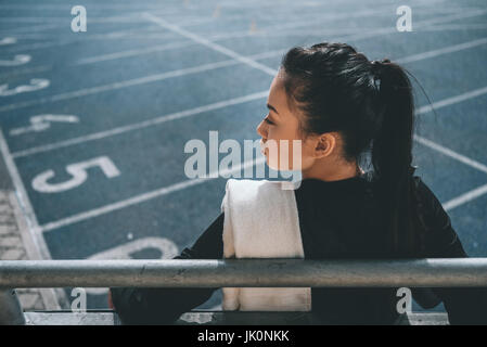 Rückansicht des asiatischen Sportlerin mit Handtuch auf Laufstrecke im Stadion Stockfoto