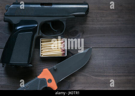 Survival-Kit für harten Mann. Schachtel Streichhölzer, klappbare Messer und schwarze Pistole auf dunklen braunen Hintergrund. Luftaufnahme der oberen Winkel Stockfoto