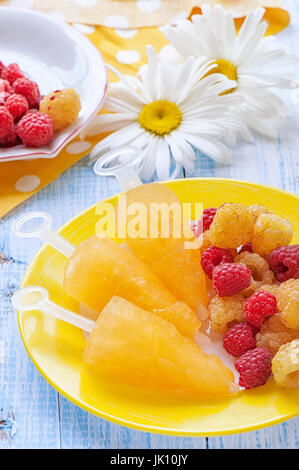 Gelbe Fruchteis gelbe Himbeeren auf einem Teller auf dem Hintergrund der Gänseblümchen. Stockfoto