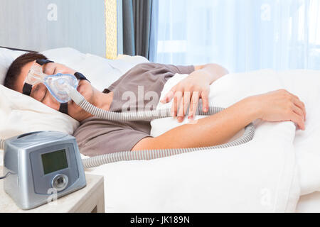 Mittelalter asiatischer Mann schläft in seinem Bett mit CPAP Maske verbinden mit Luftschlauch und CPAP-Gerät, Gerät für Menschen mit Schlafapnoe Stockfoto