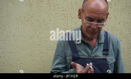 Porträt eines lächelnden Schuhmachers in Form, zur gelben Wand stehend arbeiten. Stockfoto