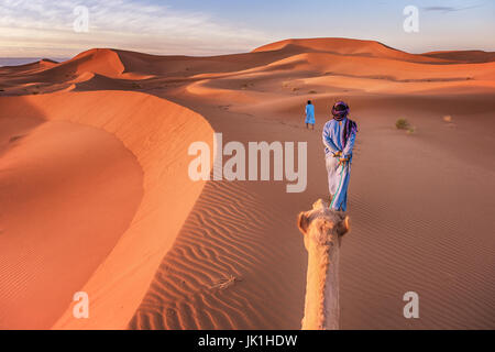 Zwei Nomaden Stammesangehörige tragen traditionelle Kleidung führen ein Kamel durch die Wüste Sahara in Marokko. Stockfoto