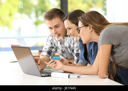 Drei Studenten, die gemeinsam auf Linie mit einem Laptop in einem Klassenzimmer lernen Stockfoto