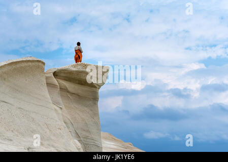 Milos, Griechenland, 17. Mai 2017: Junge Frau Tourist auf einem Felsen steht und mit Blick auf Sandstrand Sarakiniko. Insel Milos, Griechenland. Stockfoto