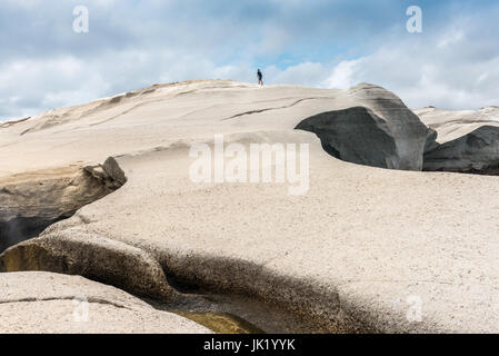 Milos, Griechenland, 17. Mai 2017: Junger Mann Tourist auf einem Felsen steht und mit Blick auf Sandstrand Sarakiniko. Insel Milos, Griechenland. Stockfoto