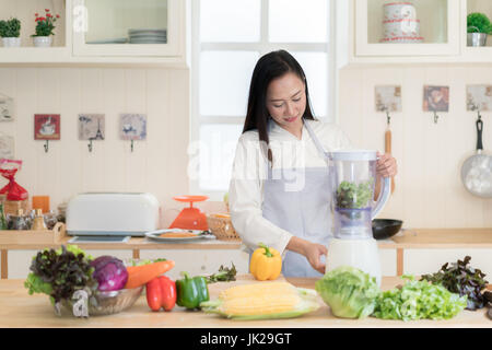 Gemüse-Smoothie. Asiatin macht grüne Smoothies mit Blender zu Hause in der Küche. Gesunden roh essen Lifestyle Konzept Porträt von schöne junge