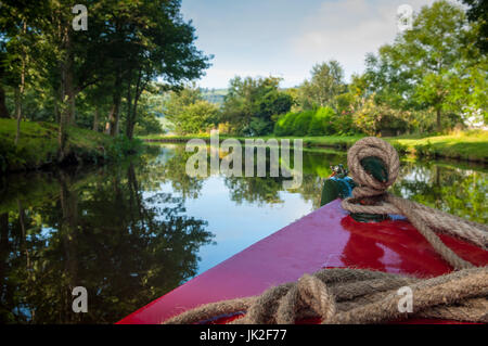 Blick vom Bug des ein Narrowboat wie es bewegt sich entlang der Leeds und Liverpool Kanal mit den Bäumen und der Bank spiegelt sich im Wasser, Yorkshire, England Stockfoto