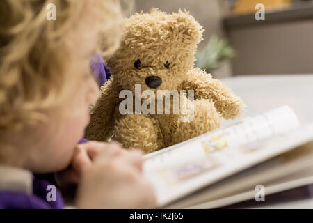Lesen Sie ein Buch mit seinem Lieblings Kindheit Teddybär kaukasischen Junge saß da und beobachtete. Stockfoto