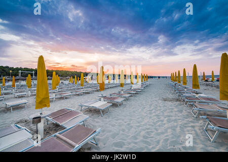 geschlossene Sonnenliegen und Sonnenschirme am Strand der Riviera der Romagna an einem Sommerabend, die Entspannung und den Charme am Meer bei Sonnenuntergang Stockfoto