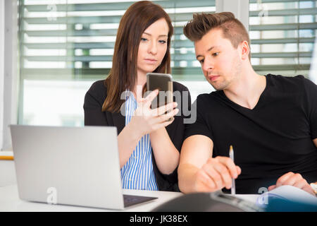 Geschäftsleute, die mit Smart Phone am Schreibtisch im Büro Stockfoto