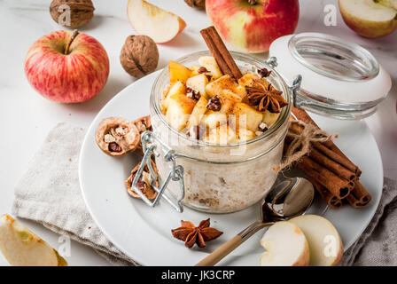 Gesunde vegane Ernährung. Diätetische Frühstück oder Snack. Apfelkuchen über Nacht Hafer, mit Joghurt, Zimt, Gewürze, Äpfel, Walnüsse. In einem Glas auf einem weißen Parketten Stockfoto