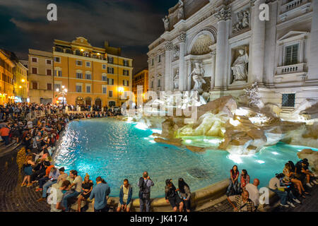 Der Trevi-Brunnen in Rom Italien beleuchtet bunt am Abend mit Touristen rund um es an einem warmen Sommerabend. Stockfoto