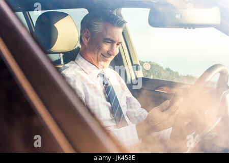 Lächelnd kaukasischen Geschäftsmann sitzen im Auto SMS auf Handy Stockfoto