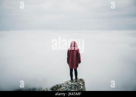 Fernen kaukasischen Frau auf Felsen beobachten Nebel am Ozean Stockfoto