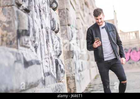 Lächelnder kaukasischen Mann zu Fuß auf dem Bürgersteig SMS auf Handy Stockfoto