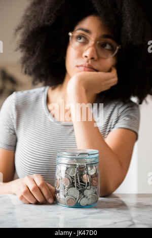 Nachdenklich afroamerikanische Frau mit Glas voller Münzen Stockfoto