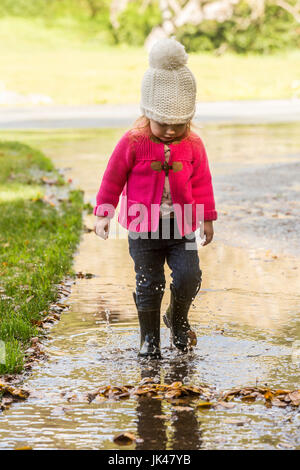 Kaukasische Mädchen tragen Stiefel in Pfütze planschen Stockfoto