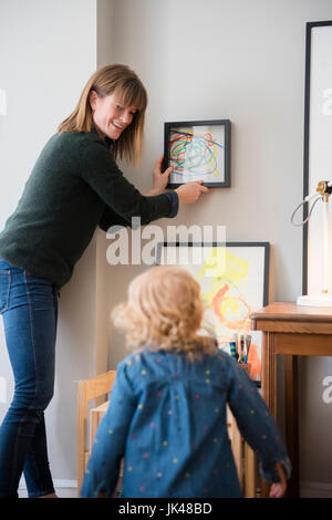 Kaukasische Mutter und Tochter, die Gemälde an der Wand hängen Stockfoto