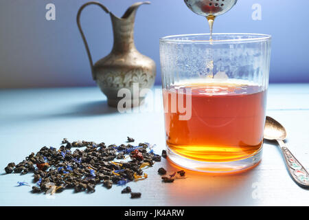Glas Tee mit Teesieb aus oberhalb der Tasse. schönes Wasser Tropfen Tee Abflüsse aus Sieb. Closeup niedrigen Winkel gedreht. Teeblätter verstreut beiseite, Dez. Stockfoto