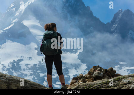 Einsame weibliche Wanderer steht auf einer Klippe in den französischen Alpen über Chamonix. Hoch, bedeckt Schnee, Berge und Wolken im Hintergrund. Stockfoto