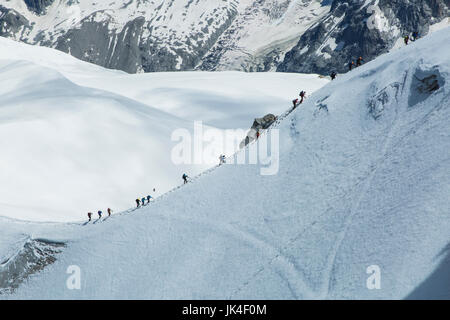 Bergsteiger klettern einen lange gefrorenen Aufstieg umgeben von Eis und Schnee mit einem Gletscher im Hintergrund am Mont Blanc Stockfoto