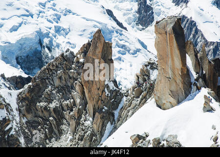 Bergsteiger klettern einen hohen Stein Höhepunkt umgeben von Eis und Schnee mit einem Gletscher im Hintergrund am Mont Blanc Stockfoto