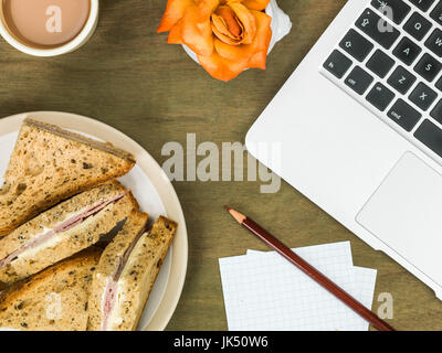 Schinken und Käse-Sandwich in dunkles Brot mit einer Tasse Tee an einem Computerarbeitsplatz Stockfoto