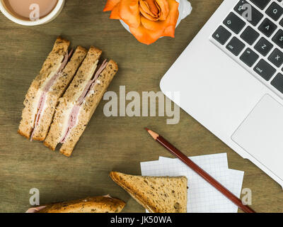 Schinken und Käse-Sandwich in dunkles Brot mit einer Tasse Tee an einem Computerarbeitsplatz Stockfoto