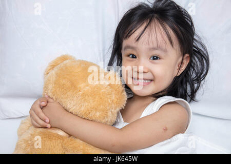 Asiatische chinesische Mädchen umarmt einen Teddybären auf dem Bett zu Hause Stockfoto