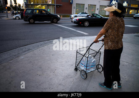 Während einer Hitzewelle transportiert eine ältere Einwanderer Frau einen Wagen voller Wasserflaschen an einer Kreuzung in Los Angeles, Kalifornien. Stockfoto