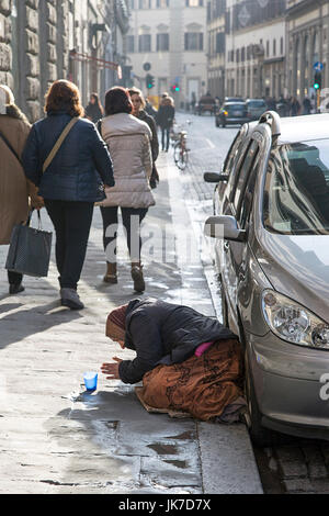 Florenz, Italien: 20. November 2016: Eine alte Frau kniet in der Florence Street betteln, während Frau vorbei mit ihren Einkaufstüten. Stockfoto