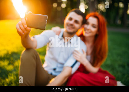 Liebespaar macht Selfie auf Handy-Kamera im Sommerpark am Sonnenuntergang. Romantisches Date attraktive Frau und junger Mann Stockfoto