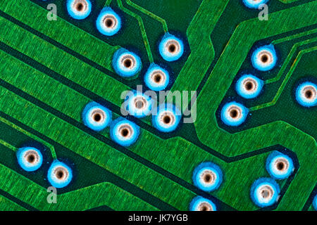 Makrofoto der Anschlussspuren auf grüner Leiterplatte (pcb) mit blauen Tauchlöchern sichtbar. Verkabelung im Computer, Details zum Schließen des Stromkreises. Stockfoto