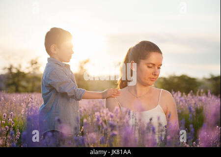 schöne Kind legte seine Hand auf die Schulter der Mutter unter Lavendelfeld Blumen im Sommer Stockfoto